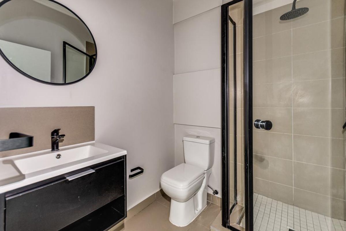 Modern bathroom featuring a sleek vanity with basin, round mirror, white toilet, and a glass-enclosed shower with contemporary black fixtures.