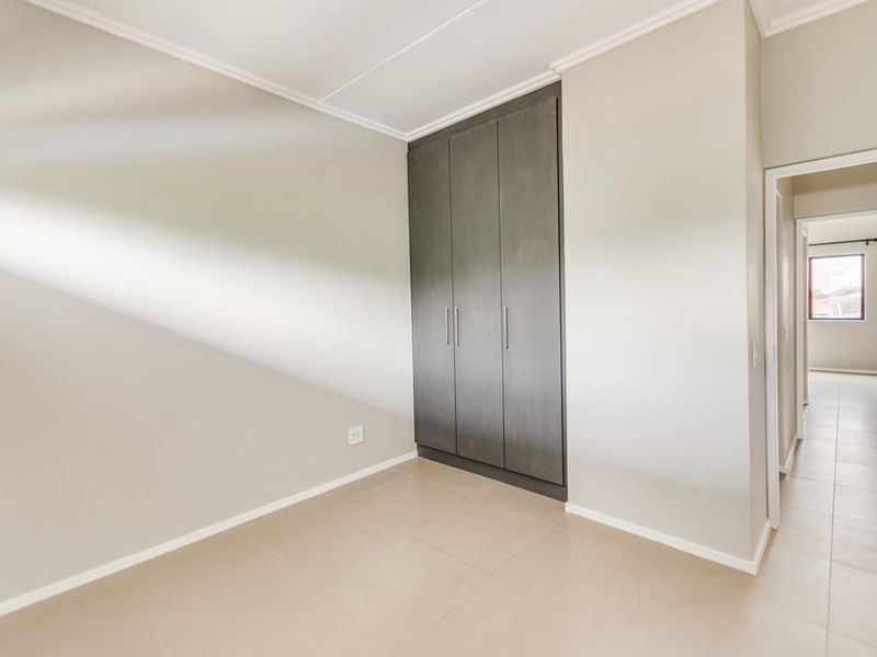 A bright, empty bedroom featuring neutral tiled flooring, modern dark built-in cupboards, and clean finishes, offering a versatile space ready for personalization.