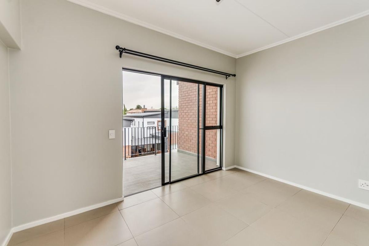 A bright, empty bedroom featuring neutral tiled flooring and a sliding glass door that opens onto a private balcony.