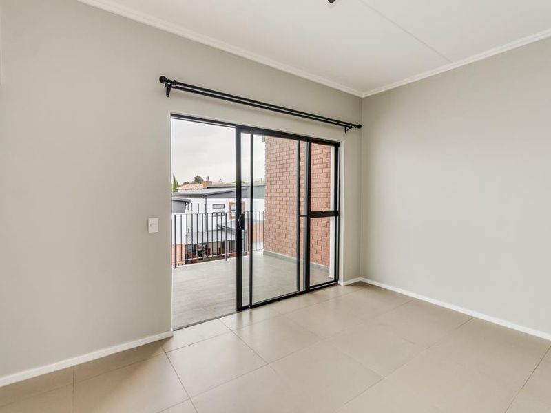 A bright, empty bedroom featuring neutral tiled flooring and a sliding glass door that opens onto a private balcony.
