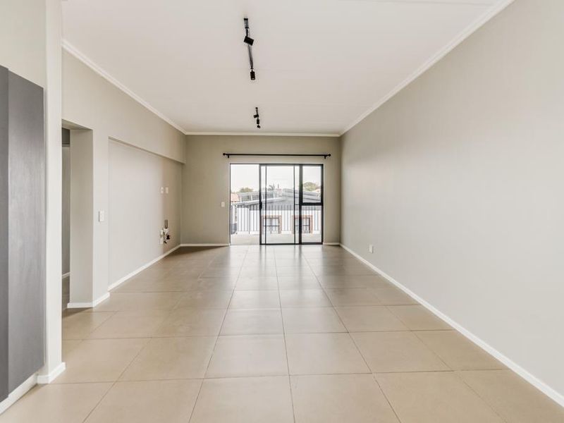 Spacious, light-filled open-plan living area featuring neutral tiled flooring, modern track lighting, and a large sliding glass door leading to an outdoor space.
