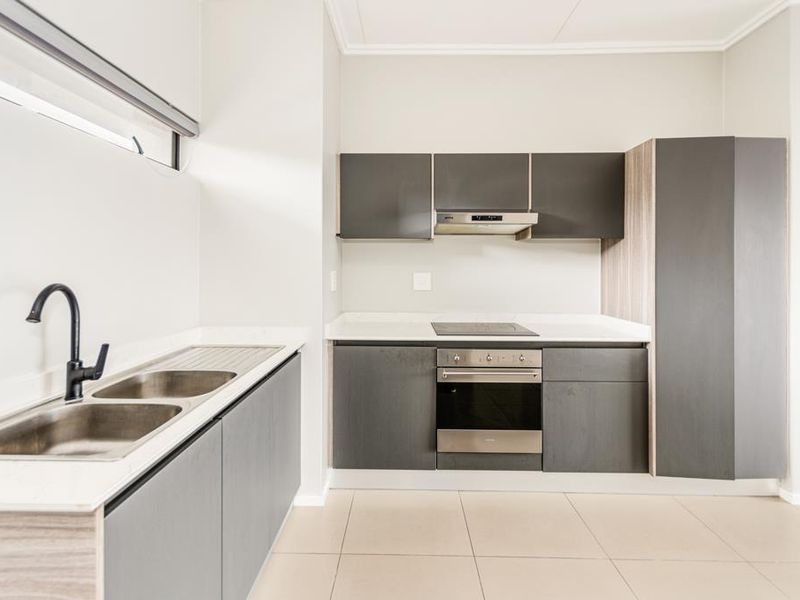 Modern kitchen featuring dark grey cabinetry, stone countertops, stainless steel sink, built-in oven, and electric hob with extractor fan.