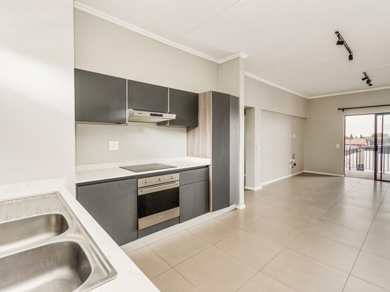 Modern open-plan kitchen and living area featuring sleek dark cabinetry, integrated appliances, stone countertops, tiled floors, and access to a private balcony.