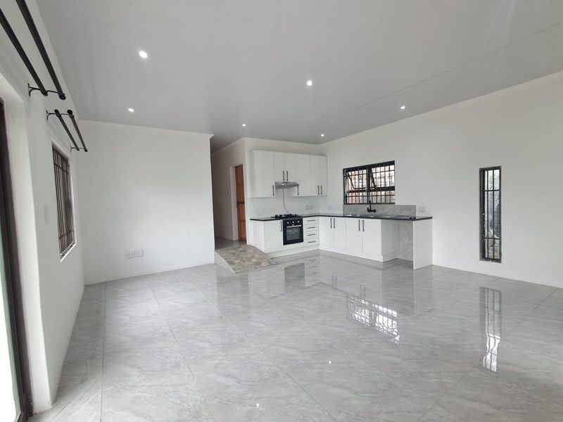 Spacious open-plan living area featuring modern white kitchen cabinetry, integrated appliances, sleek porcelain floor tiles, and recessed lighting throughout.