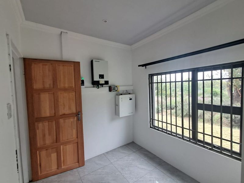 A clean utility space featuring tiled flooring, a wooden door, and installed solar power infrastructure including an inverter and battery system.