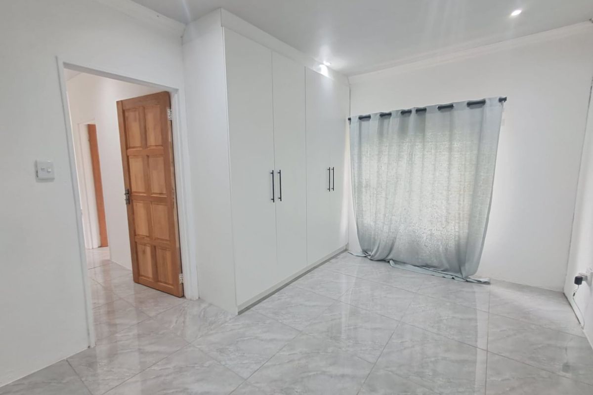A bright, empty bedroom featuring modern grey tiled flooring, built-in white cupboards, and recessed ceiling lighting.