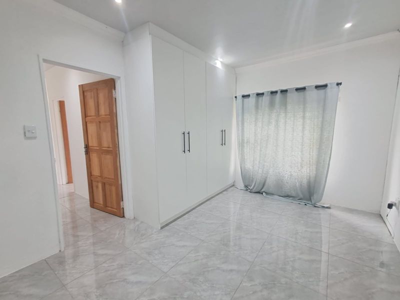 A bright, empty bedroom featuring modern grey tiled flooring, built-in white cupboards, and recessed ceiling lighting.