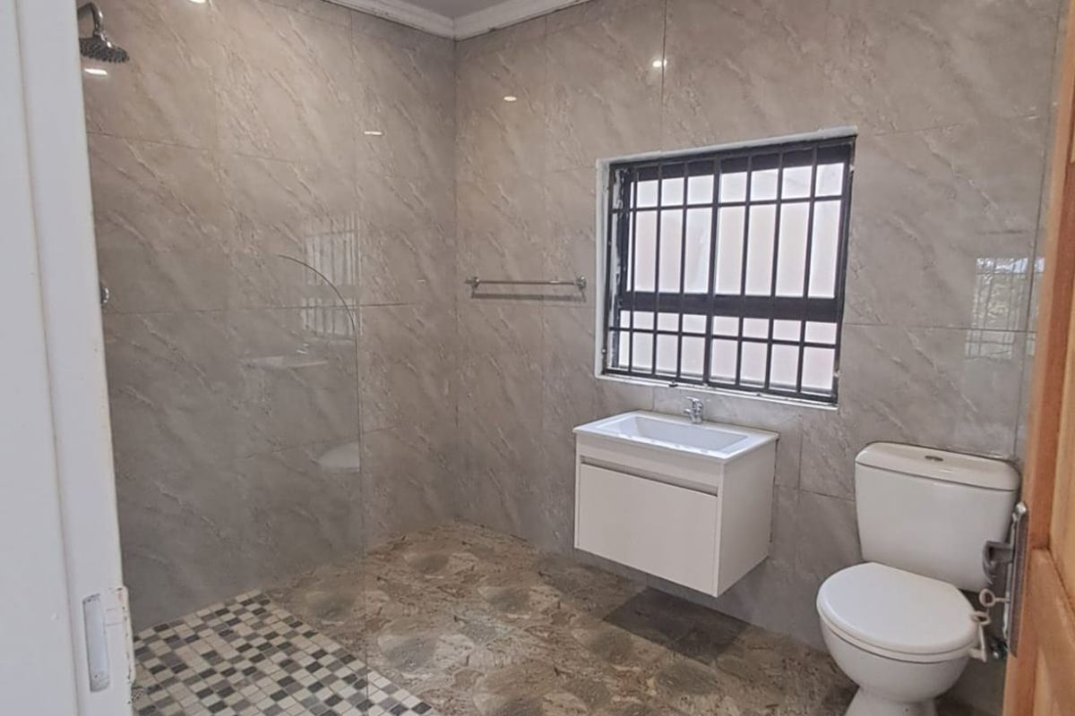 A clean, modern bathroom featuring a walk-in shower with glass screen, wall-mounted vanity, and neutral floor-to-ceiling tiling.