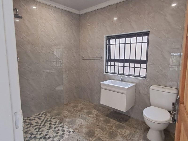 A clean, modern bathroom featuring a walk-in shower with glass screen, wall-mounted vanity, and neutral floor-to-ceiling tiling.