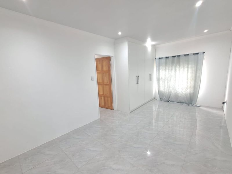 A bright, empty bedroom featuring modern tiled flooring, built-in cupboards, and recessed downlighting, providing a clean and neutral space ready for personalization.