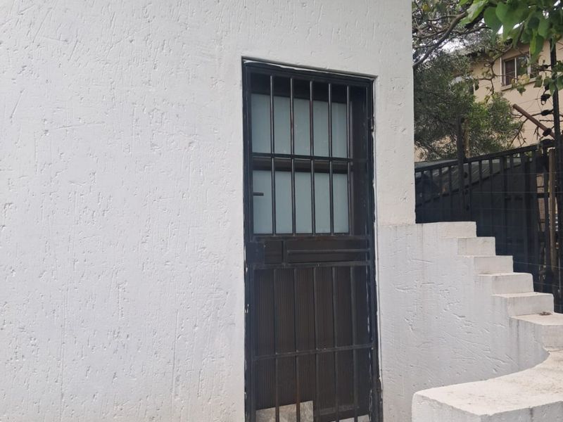 Exterior view of a rear building entrance featuring a security gate, textured plaster walls, and concrete steps leading to the doorway.