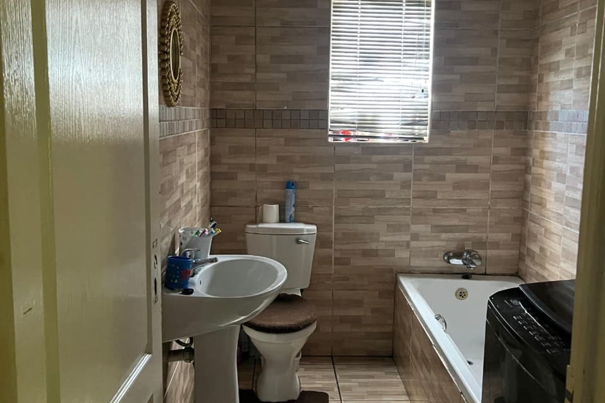 A functional bathroom featuring a pedestal basin, toilet, and bathtub with full-height wall tiling and tiled flooring.