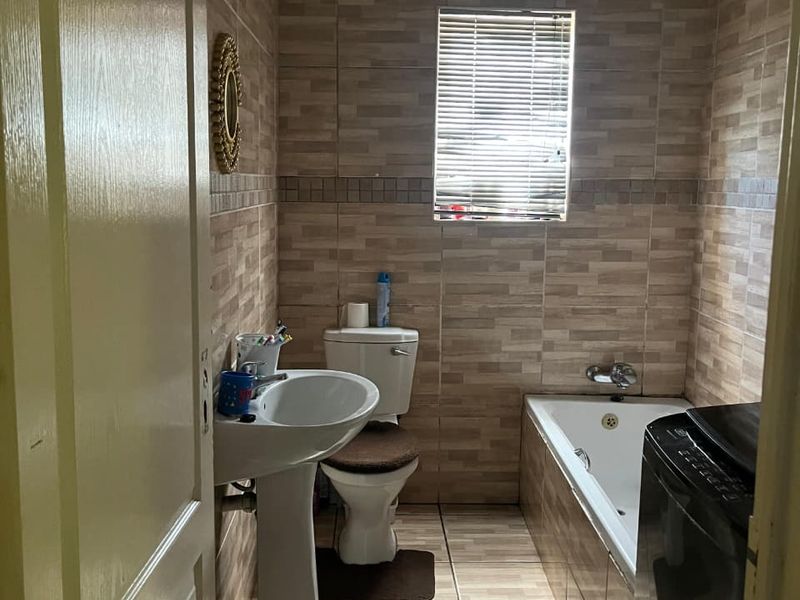 A functional bathroom featuring a pedestal basin, toilet, and bathtub with full-height wall tiling and tiled flooring.