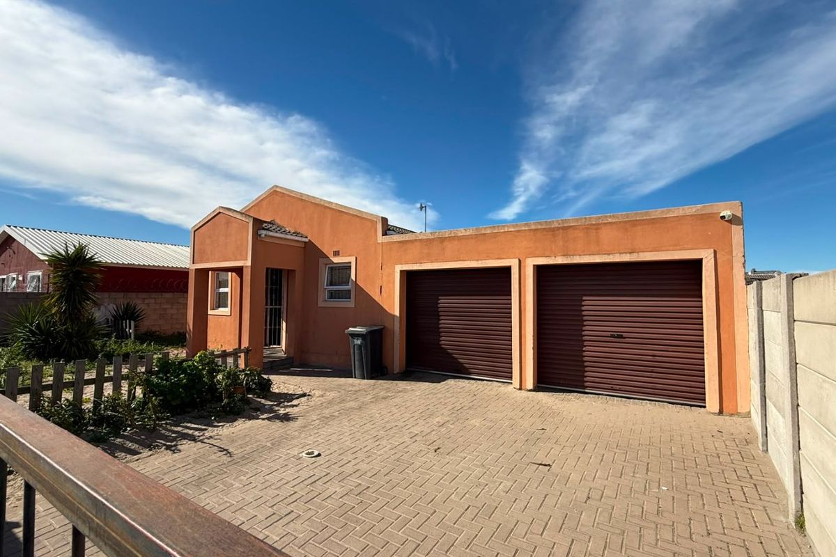 Front elevation of a residential house featuring a double garage, paved driveway, and secure boundary walling.