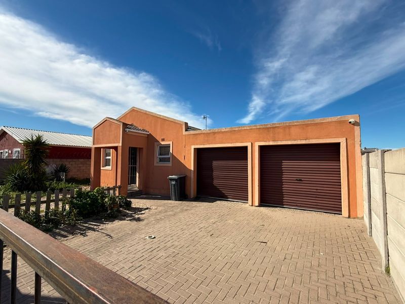 Front elevation of a residential house featuring a double garage, paved driveway, and secure boundary walling.