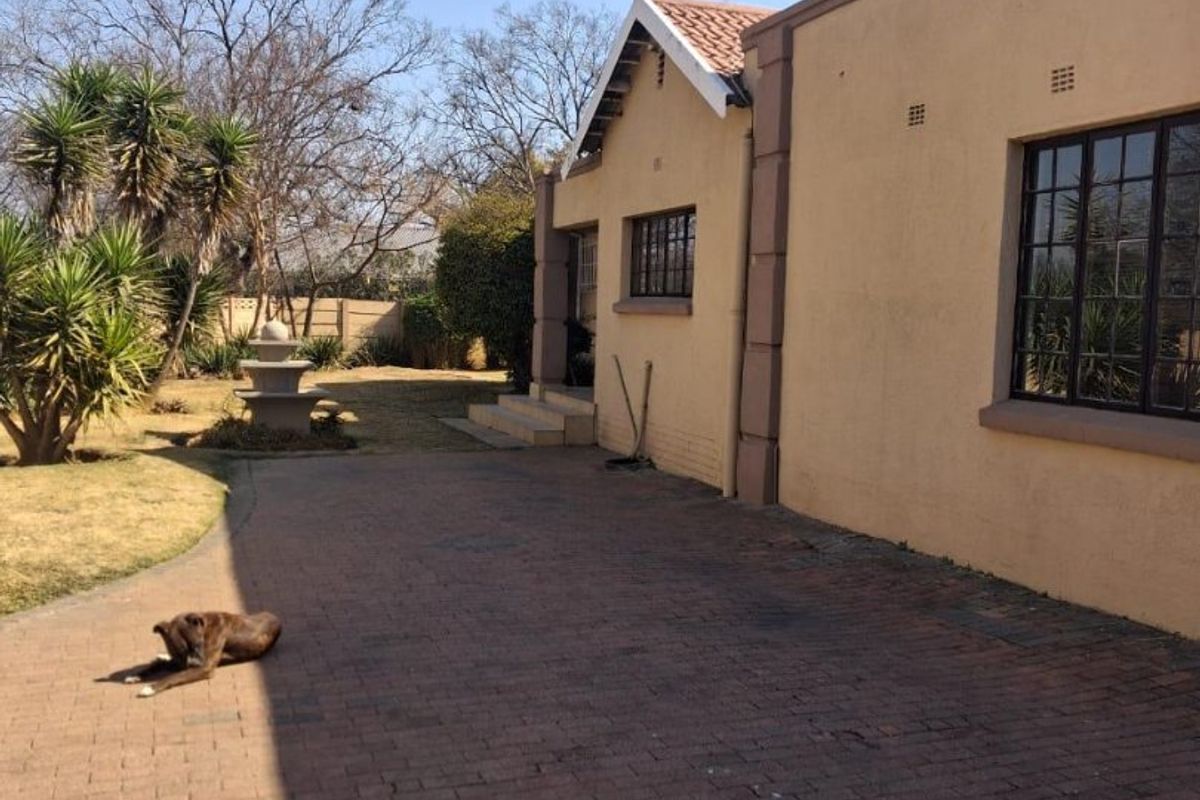 Rear exterior view of the property featuring a paved driveway, established garden with a stone fountain, and traditional tiled roof architecture.