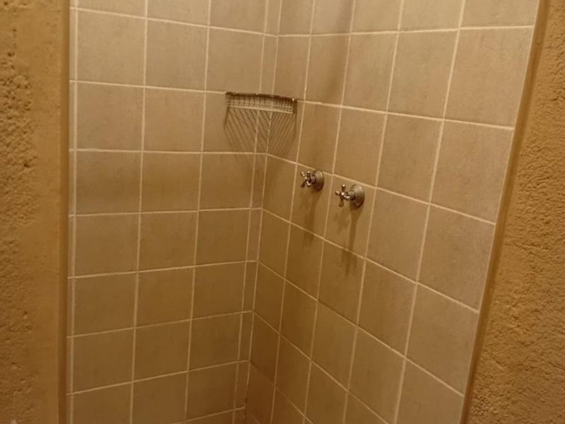A compact shower enclosure featuring neutral wall tiles and a mosaic tiled floor, equipped with standard chrome mixer taps.