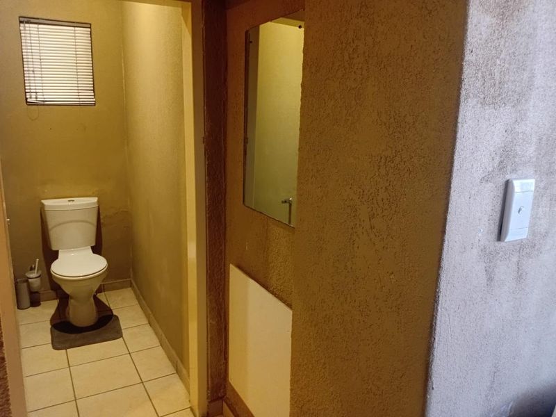 A compact bathroom featuring a standard toilet, tiled flooring, and a wall-mounted mirror, requiring cosmetic updates to improve the overall finish.