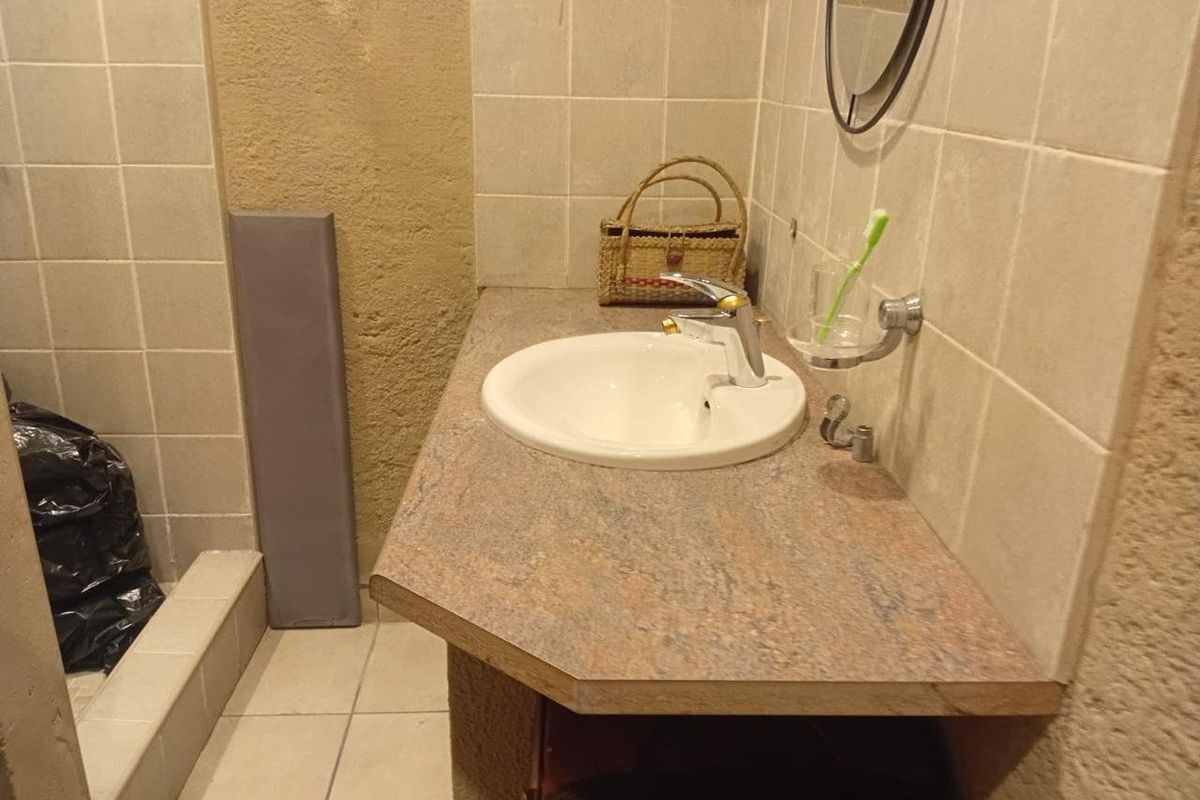 A compact bathroom featuring a vanity basin with a laminate countertop, tiled splashback, and a shower enclosure with tiled walls.