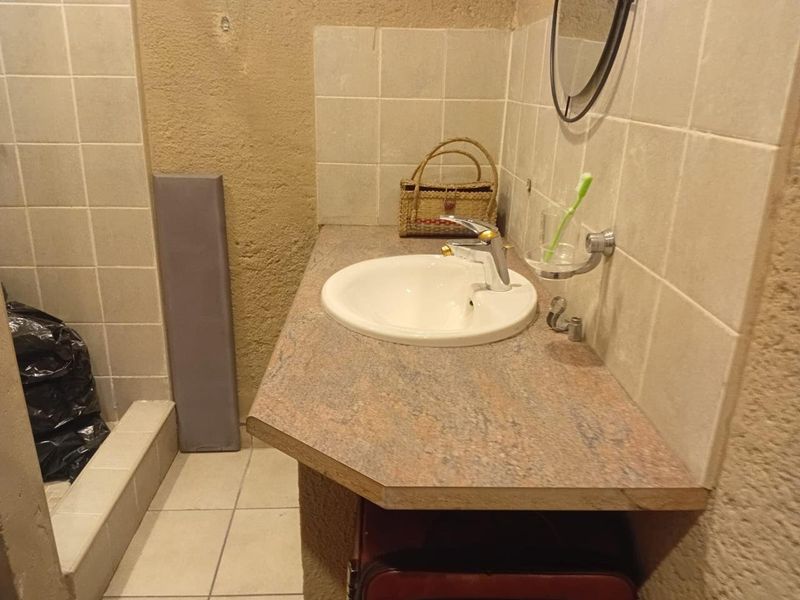 A compact bathroom featuring a vanity basin with a laminate countertop, tiled splashback, and a shower enclosure with tiled walls.