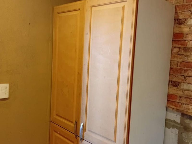A kitchen area featuring built-in cabinetry and an exposed brick wall, currently showing signs of wear and unfinished wall surfaces.