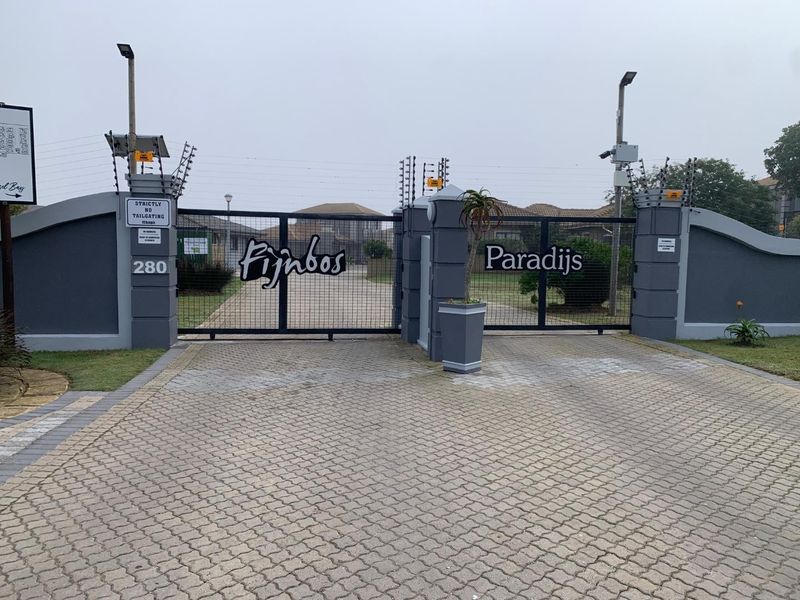 Secure gated entrance to Fijnbos Paradijs complex featuring paved driveway, masonry pillars, and integrated electric security fencing.