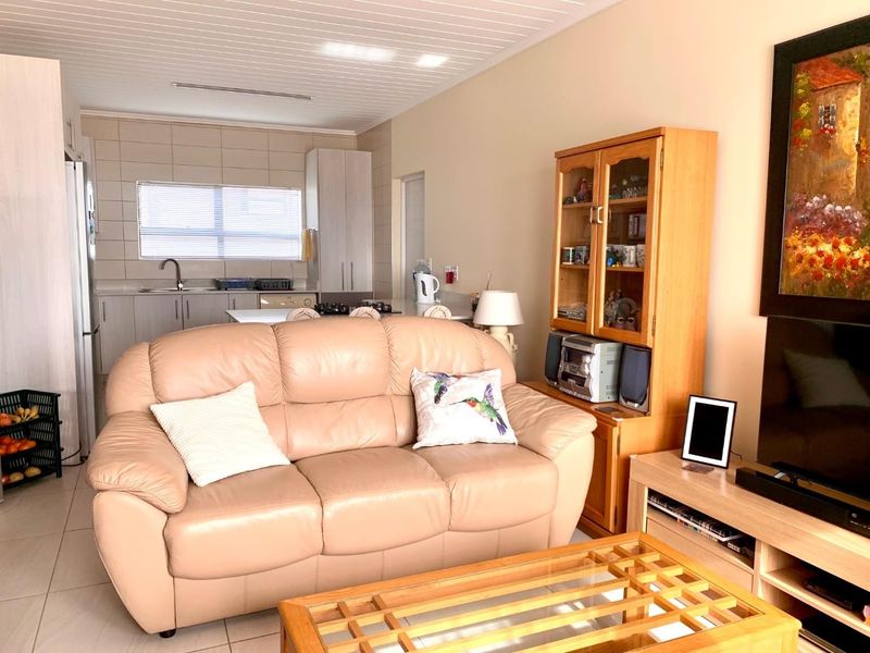 An open-plan living area featuring a combined kitchen with tiled backsplash and cabinetry, flowing into a comfortable lounge space with tiled flooring.