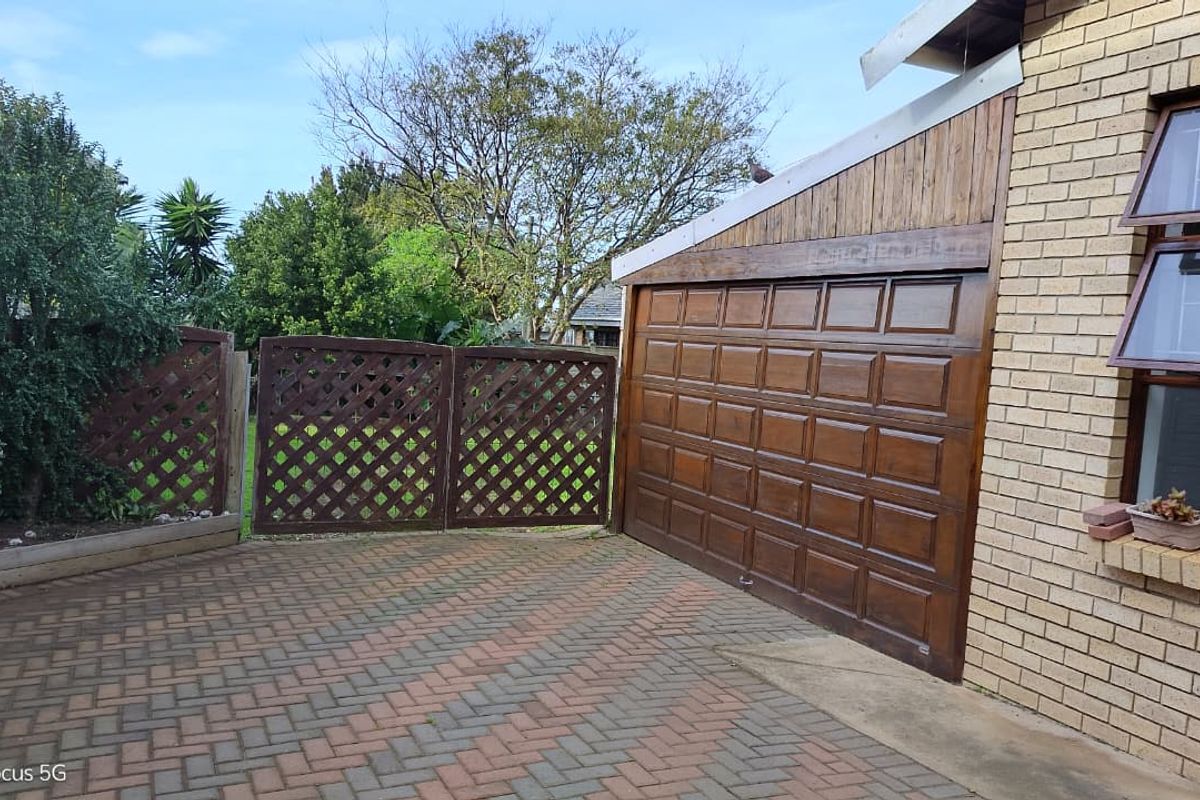 Rear exterior view featuring a paved driveway, wooden garage door, and decorative trellis fencing against a brick building facade.
