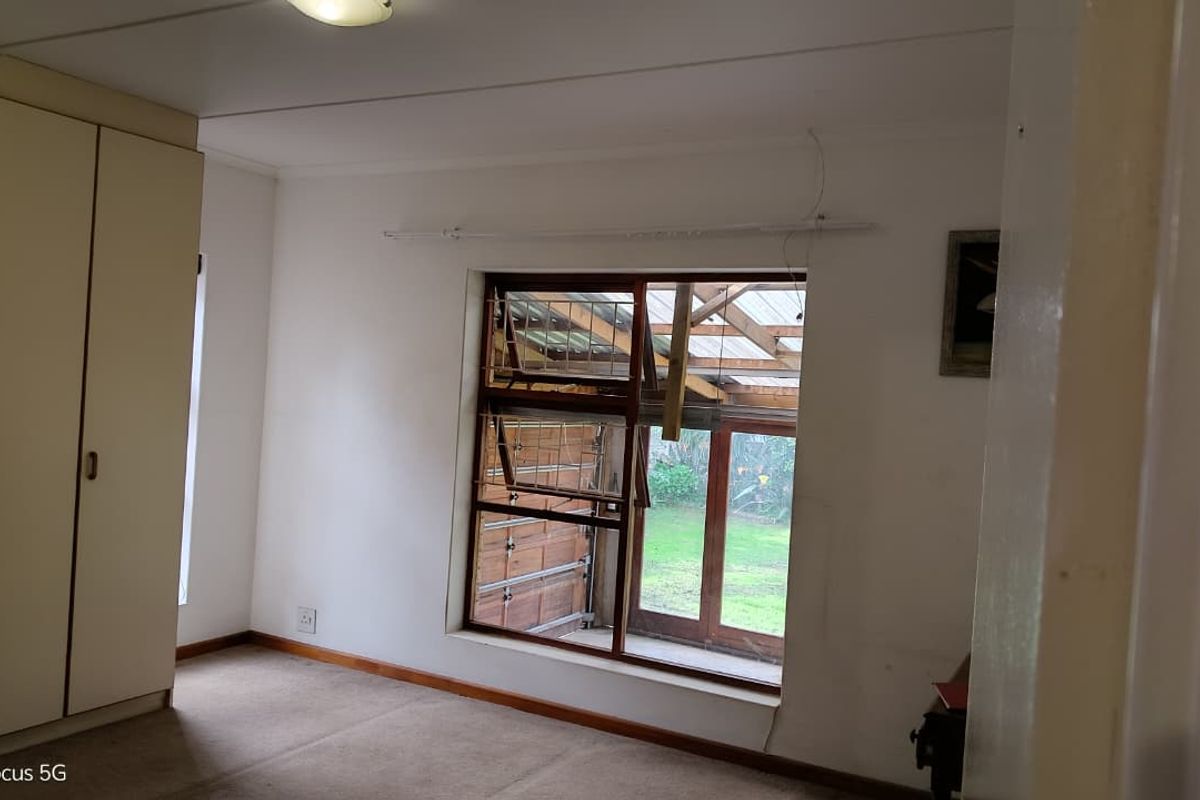 A vacant bedroom featuring built-in cupboards, carpeted flooring, and a timber window frame looking out onto a covered patio area.