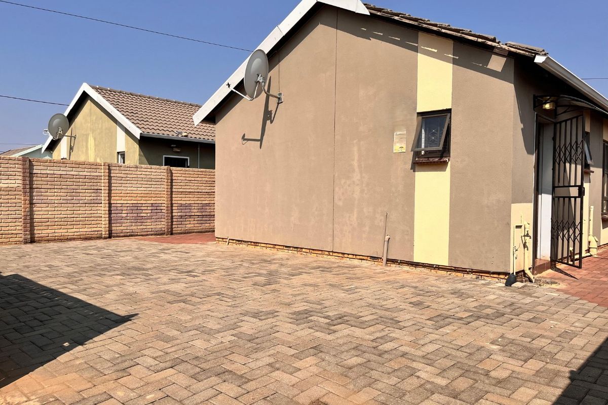 Rear exterior view of the property featuring a paved courtyard area, brick boundary wall, and security gate access.