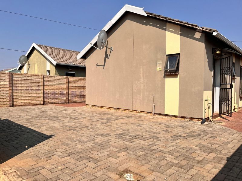 Rear exterior view of the property featuring a paved courtyard area, brick boundary wall, and security gate access.