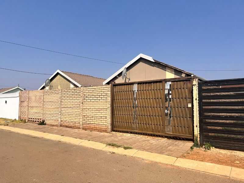 Street view of a residential property featuring a brick boundary wall, a metal sliding gate, and a paved driveway entrance.