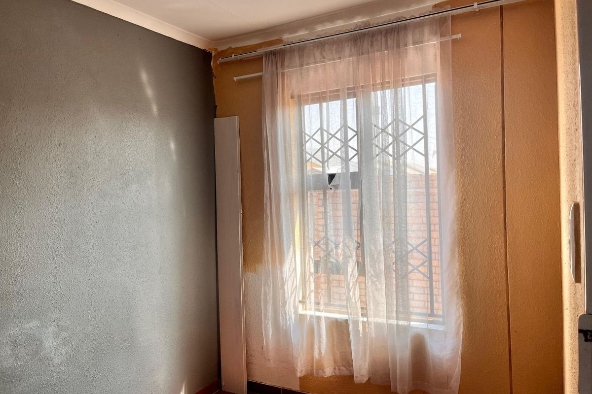 An empty bedroom featuring tiled flooring, a window with a security gate, and partially painted walls requiring finishing touches.