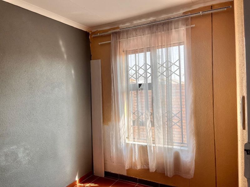 An empty bedroom featuring tiled flooring, a window with a security gate, and partially painted walls requiring finishing touches.
