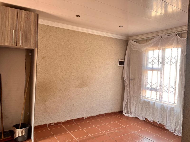 An empty kitchen area featuring tiled flooring, built-in cabinetry, and a window with security bars, ready for renovation or modernization.