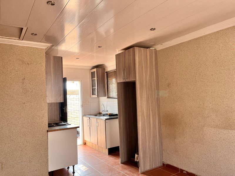 A compact kitchen featuring wood-look cabinetry, tiled flooring, and recessed lighting, currently vacant and in need of cosmetic updates to the wall finishes.