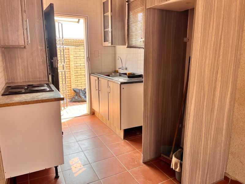 A functional kitchen featuring built-in cabinetry, an electric hob, and tiled flooring, with direct access to an outdoor area.