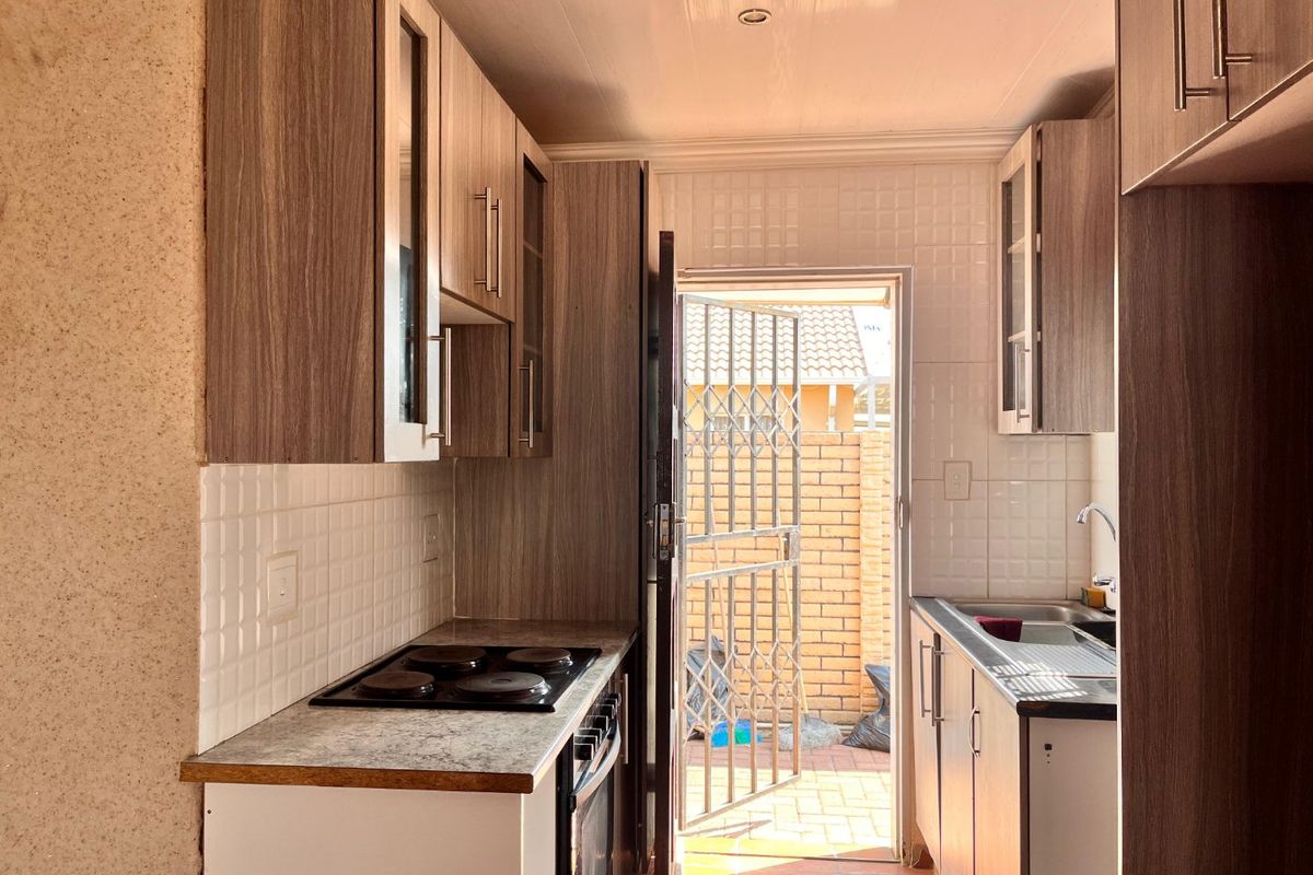 Compact kitchen featuring wood-look cabinetry, electric hob, built-in oven, and direct access to an exterior paved courtyard area.