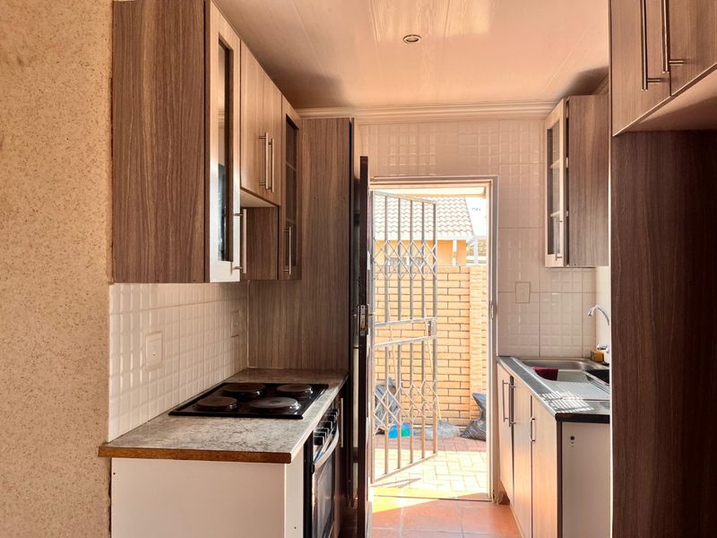 Compact kitchen featuring wood-look cabinetry, electric hob, built-in oven, and direct access to an exterior paved courtyard area.
