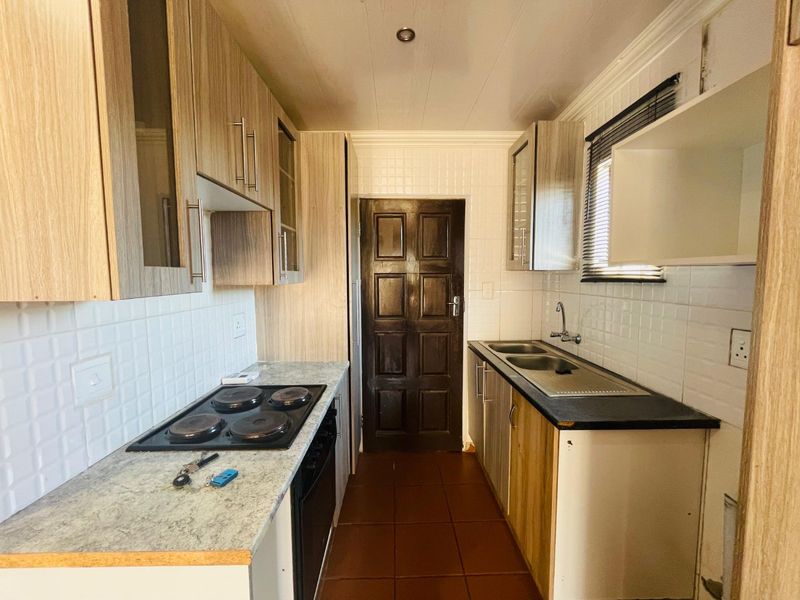A functional galley-style kitchen featuring wood-look cabinetry, laminate countertops, an integrated electric hob and oven, and a double sink with tiled splashbacks.