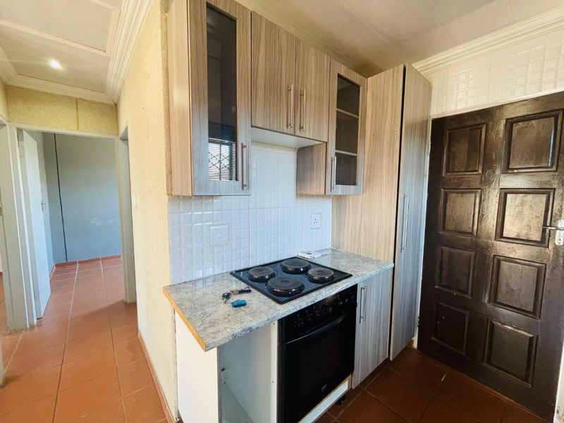 Compact kitchen featuring built-in cabinetry, an electric hob, oven, and tiled backsplash, with direct access to the hallway.