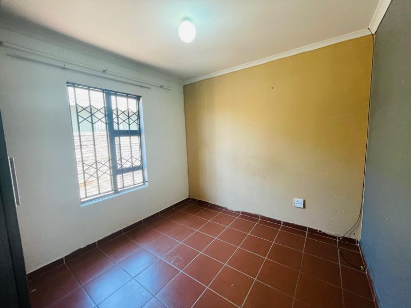 An empty bedroom featuring tiled flooring, a security gate on the window, and a neutral wall finish, ready for personalization.