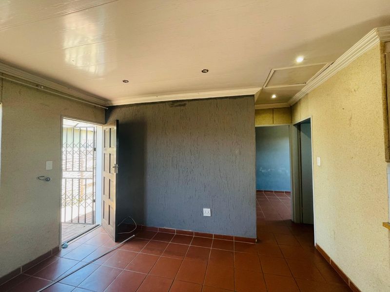 An empty living area featuring tiled floors, recessed lighting, and a textured feature wall, providing a blank canvas for potential interior updates.