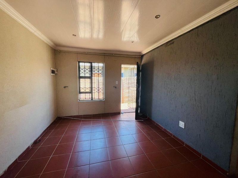 An empty living room featuring red tiled flooring, a textured accent wall, recessed lighting, and direct access to an outdoor area via a security gate.