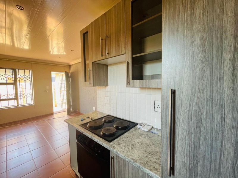 A functional kitchen featuring wood-look cabinetry, granite-effect countertops, an integrated electric hob and oven, and direct access to an outdoor area.