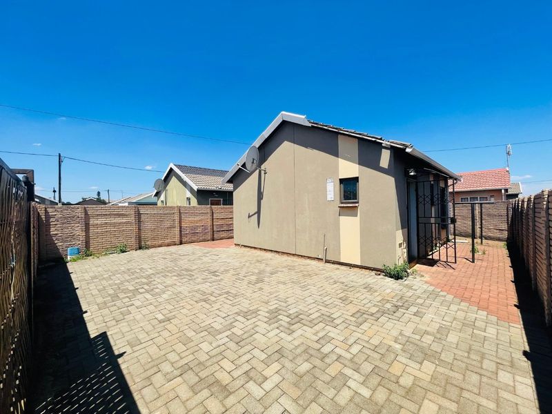 Rear exterior view of the property featuring a paved courtyard, brick boundary walls, and a secure entrance gate.
