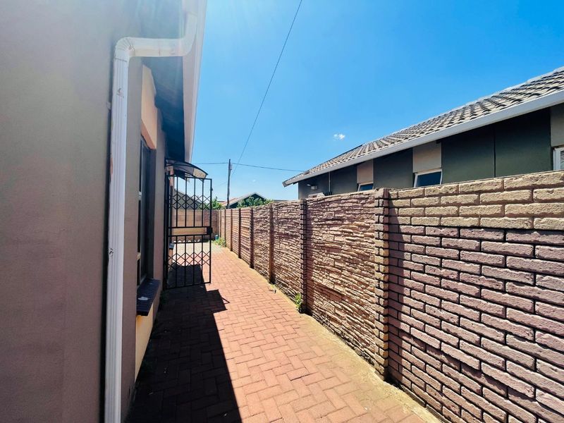 A side passage featuring a paved walkway, a textured brick boundary wall, and a secure metal gate.