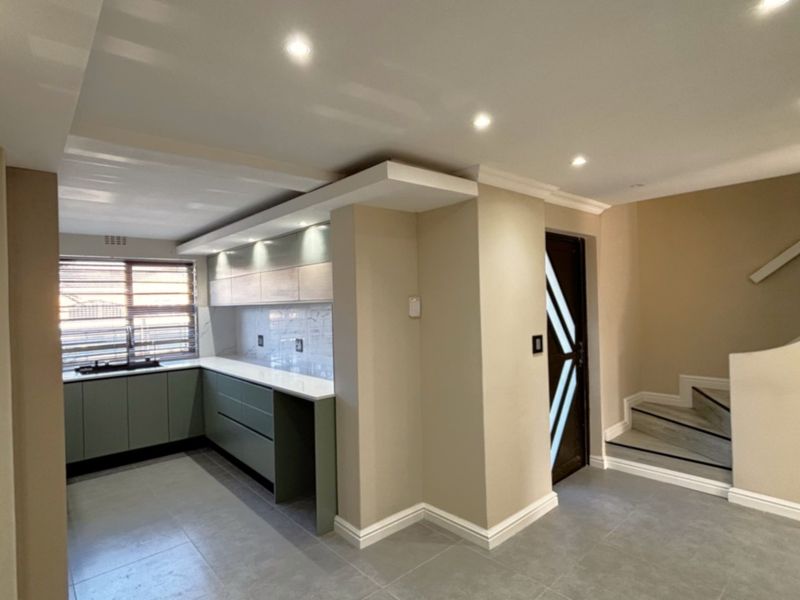 Modern kitchen featuring sleek built-in cabinetry, stone countertops, and recessed lighting, adjacent to a staircase with tiled flooring throughout.