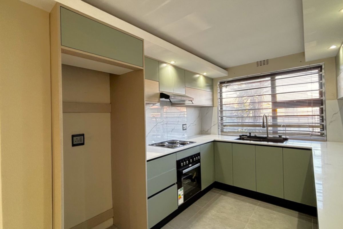 Modern, renovated kitchen featuring sage green cabinetry, stone countertops, integrated appliances, and a marble-look splashback with ample natural light.