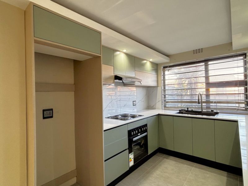 Modern, renovated kitchen featuring sage green cabinetry, stone countertops, integrated appliances, and a marble-look splashback with ample natural light.
